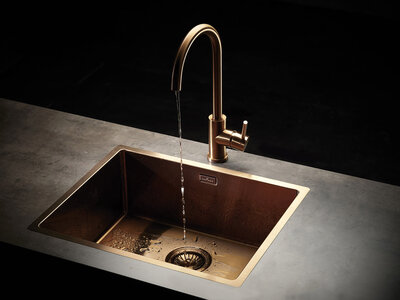Výrazné kontrasty mezi temnými matnými povrchy kování a lesklými mosaznými, měděnými nebo zlatavými tóny u kuchyňských dřezů a baterií efektně doplňují různé styly nábytku Mosazný dřez s puštěnou baterií